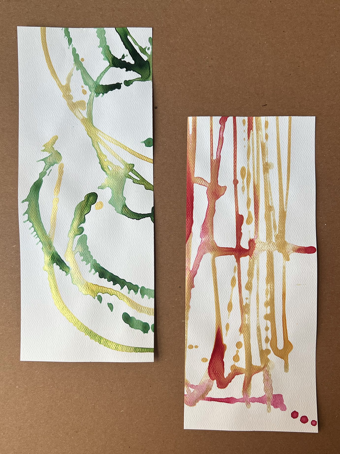 The image is two pieces of off-set white watercolor paper. The first and higher image is on the viewer's left side, and has green and gold streaks of watered-down green and gold acrylic paint splattered in arcs. The second is lower on the right, with red and gold watered down acrylic paint splattered in intersecting grids.